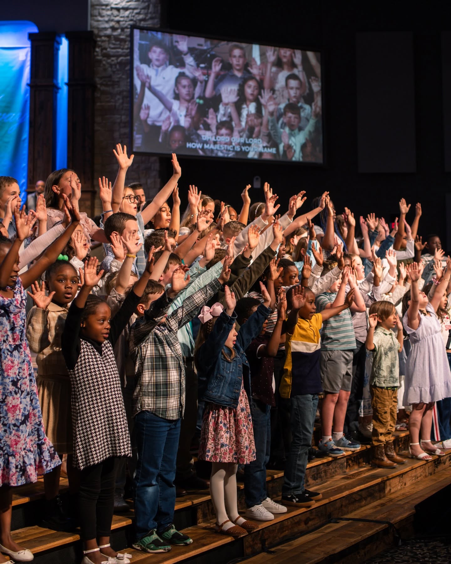 Children standing on risers with hands raised in worship