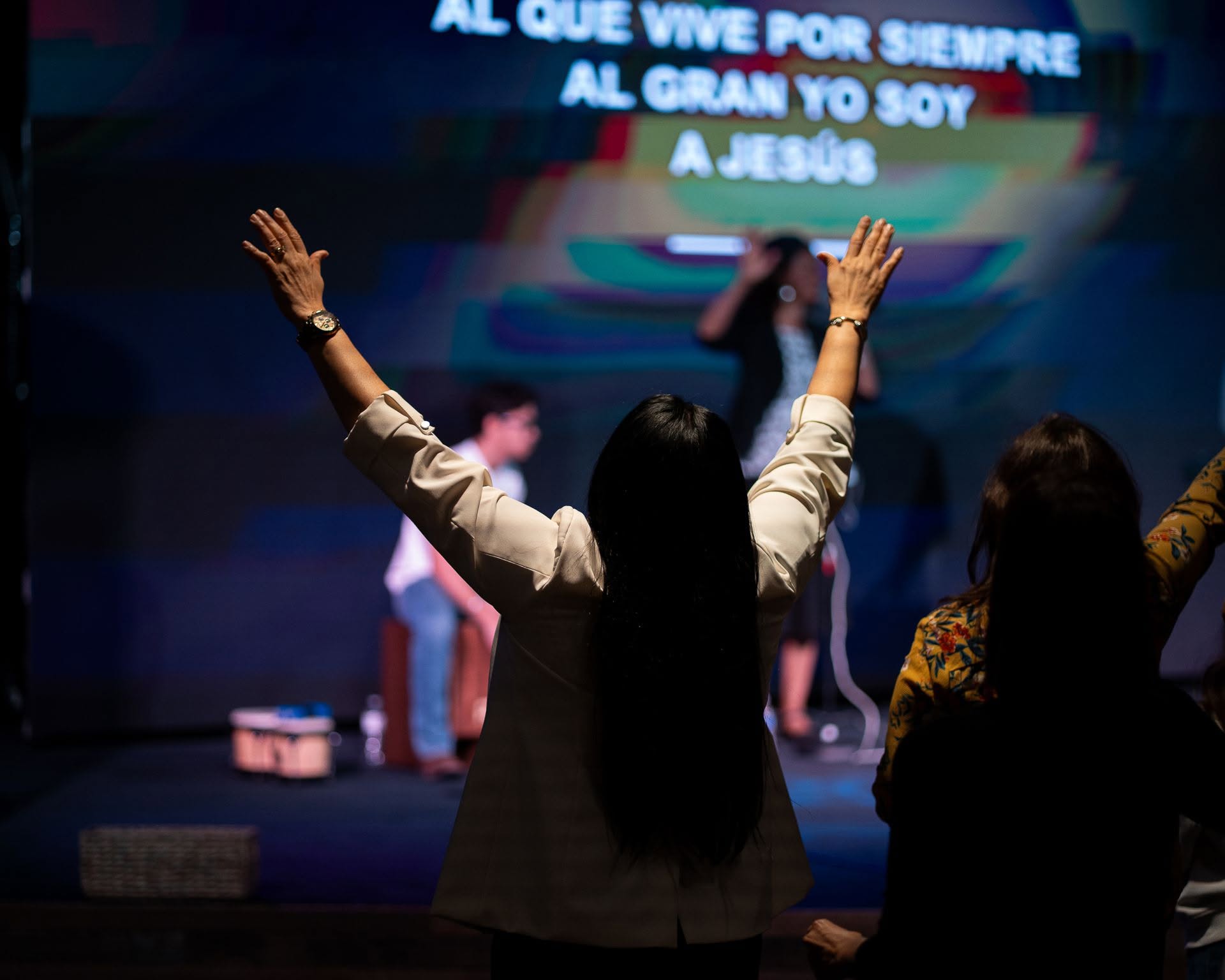 A woman worshipping with both hands raised as Spanish lyrics appear on the screen
